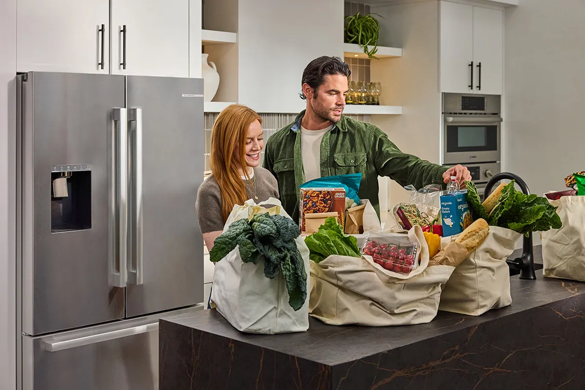 Couple unpacking groceries next to a Bosch refrigerator