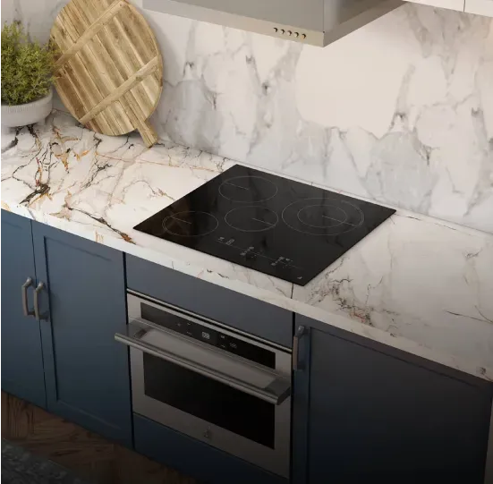 Black glass electric cooktop with four circular heating zones and front touch controls, flush-mounted in a white marble countertop above a built-in oven and blue cabinets.