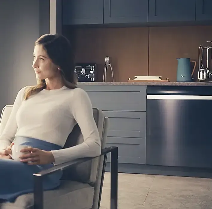 lady sitting in front of dishwasher peacefully, showcasing whisper quiet cleaning.