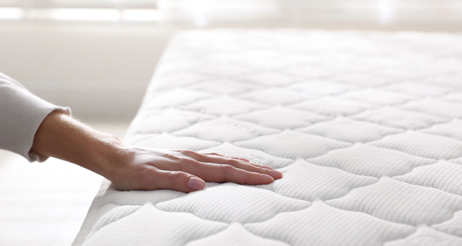 Hand pressing into a soft mattress surface to test how it feels