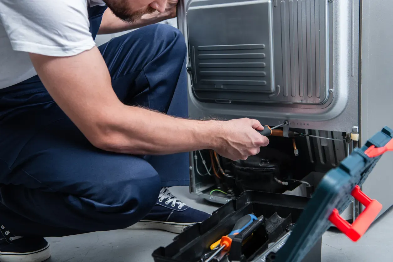 A technician inspects the back of a refrigerator in a home kitchen.