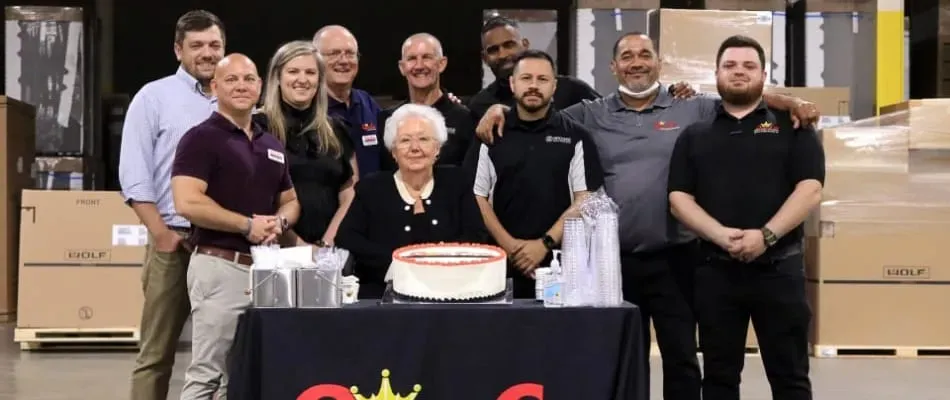 Queen City team standing in front of a table with their logo and a cake