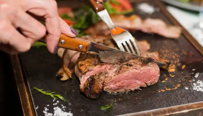 A knife and fork cut up a well cooked steak.