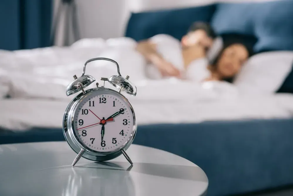 Alarm-clock-on-table-couple-in-bed-in-background