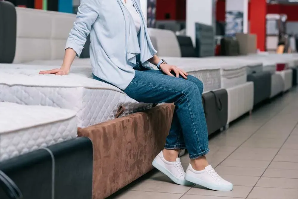 Woman-wearing-jeans-and-sneakers-sitting-on-a-mattress-at-a-mattress-store