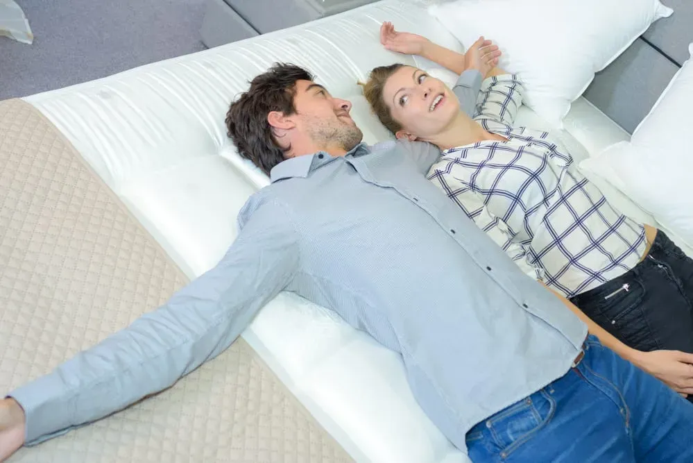 Young-couple-laying-on-mattress-at-store-smiling