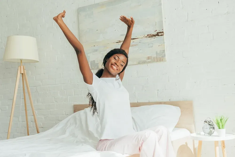 Young-smiling-woman-stretching-arms-sitting-on-bed