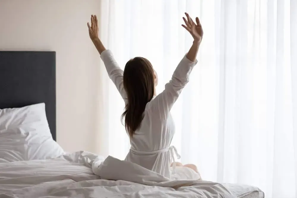 Young-woman-in-white-robe-stretching-in-bed