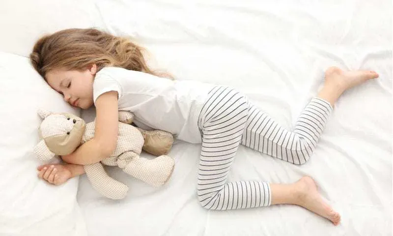 young-girl-holding-a-teddy-bear-asleep-on-white-sheets
