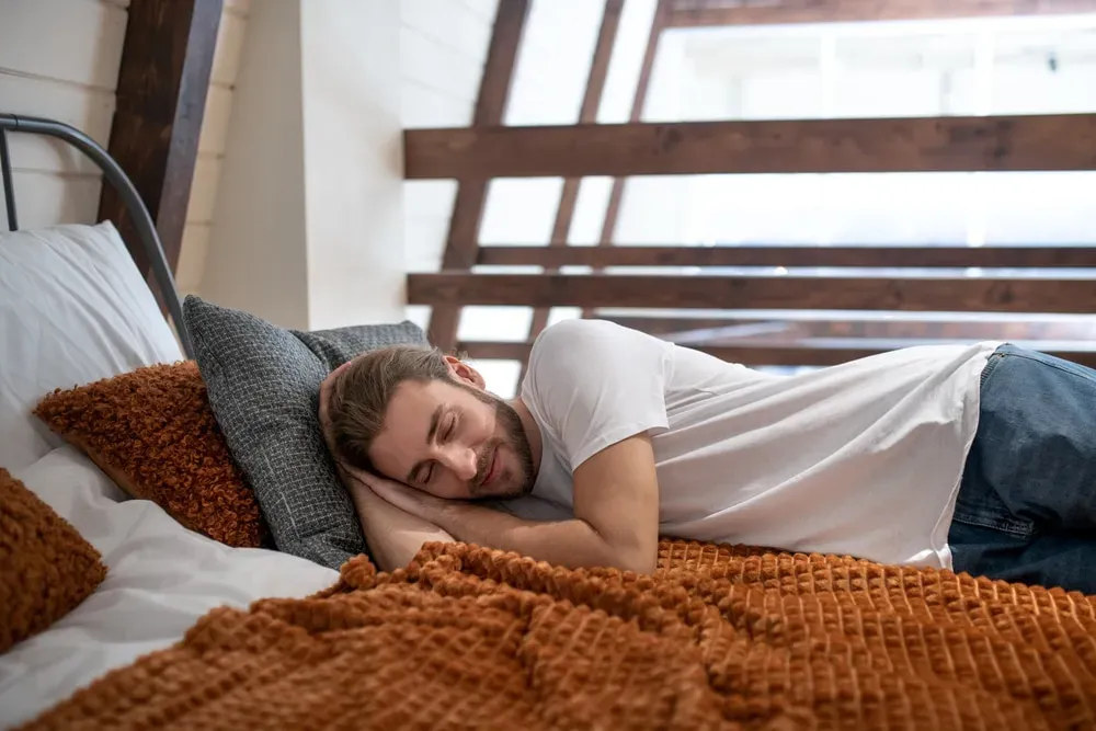 Young man happily napping on top of blanket in bed