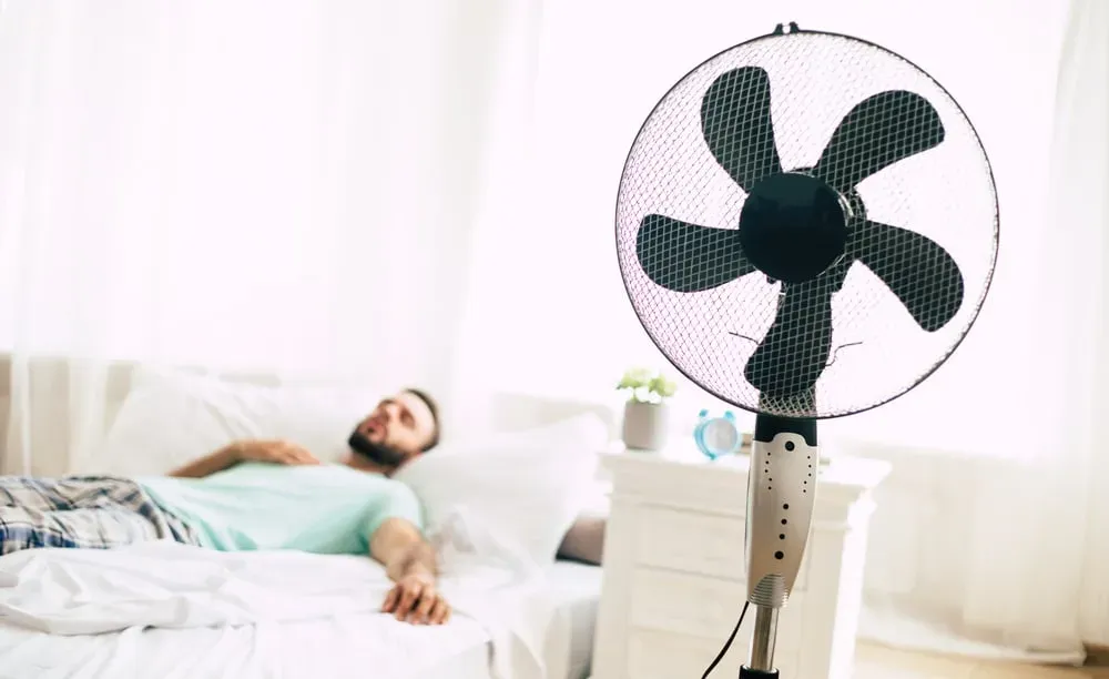 Young-man-lying-in-bed-looking-hot-fan-in-foreground