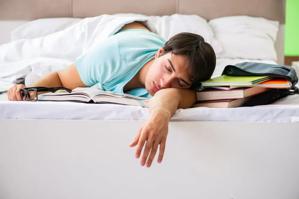 Young man studying and sleeping in bed