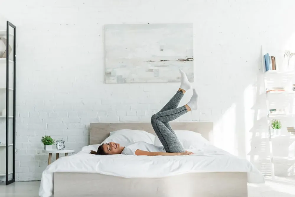 Young smiling woman lying on bed with her feet in the air