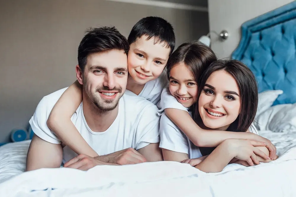 Happy family smiling and cuddling in bed, parents and 2 kids