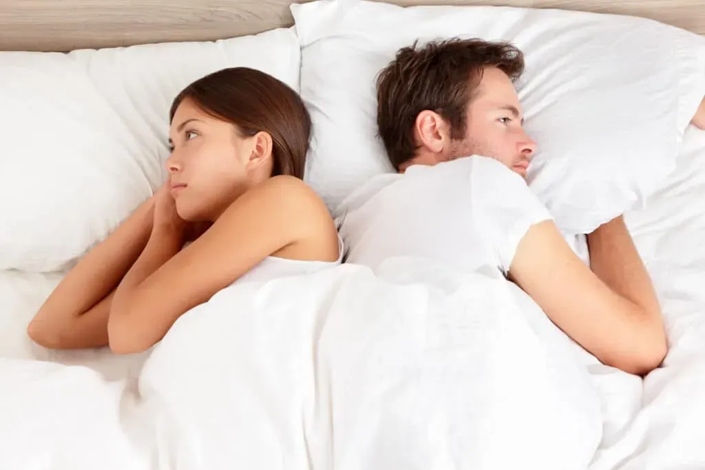 Young couple in bed facing opposite directions
