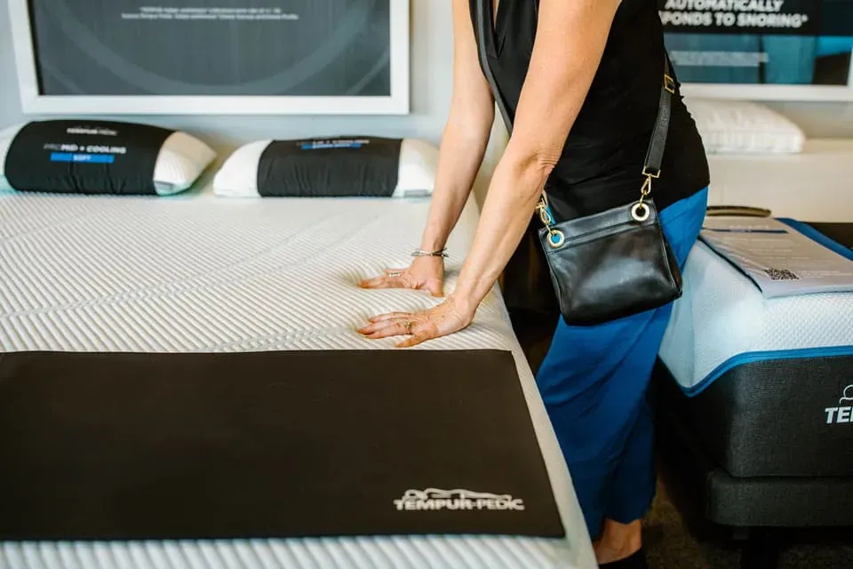 a woman testing the firmness of a mattress by leaning on it with her hands