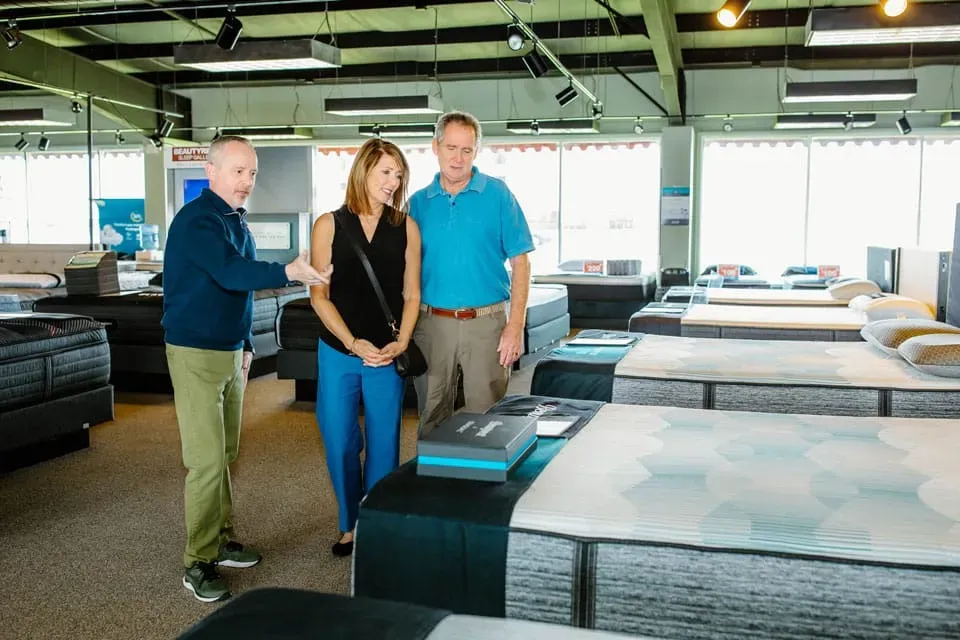 Store clerk showing mattresses to a man and woman.