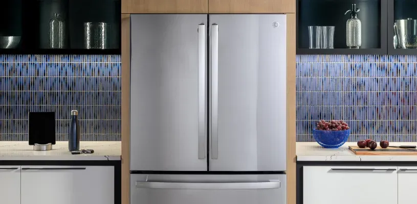 kitchen with white cabinets and a colorful, blue-tiled backspalsh and a large, brushed stainless steel refrigerator in the middle of the image.