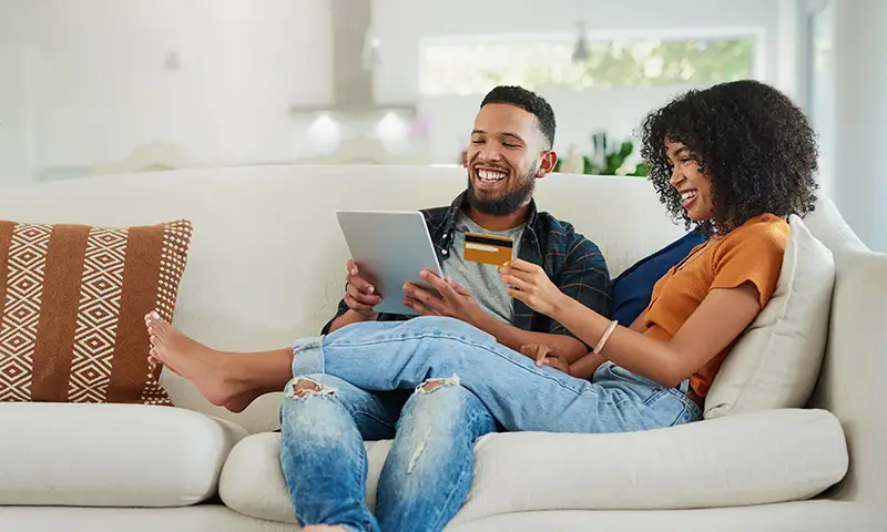 Two people sitting on a couch shopping online with a laptop and a credit card